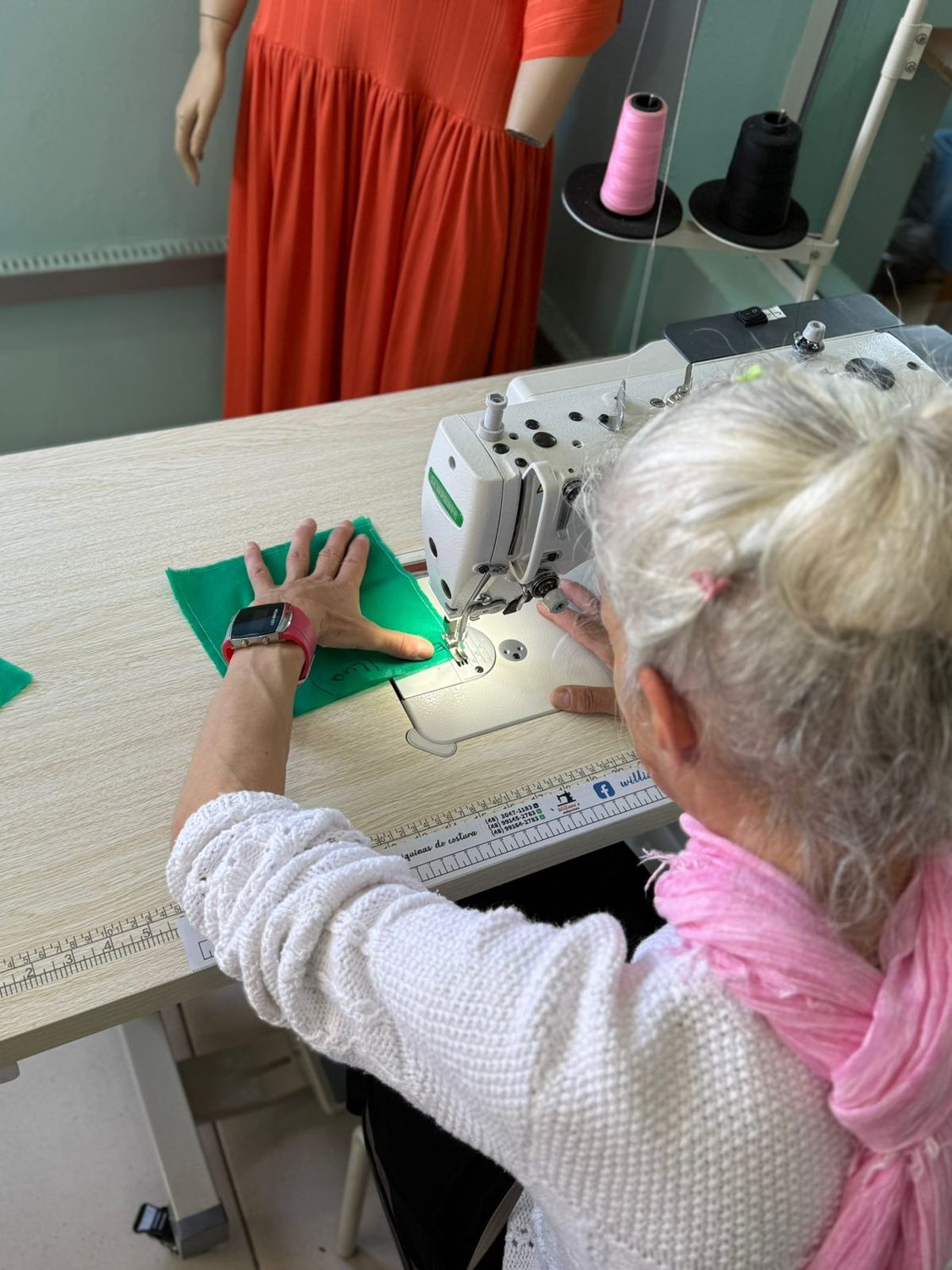 Mulher costurando tecido verde em máquina industrial